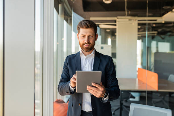 istock Happy male entrepreneur using digital tablet and smiling, standing near window at modern coworking office, copy space 1478505200
