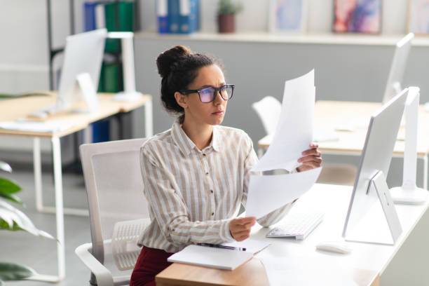 istock Concentrated latin businesswoman working with documents and reports, sitting at workplace in office interior 1478505210