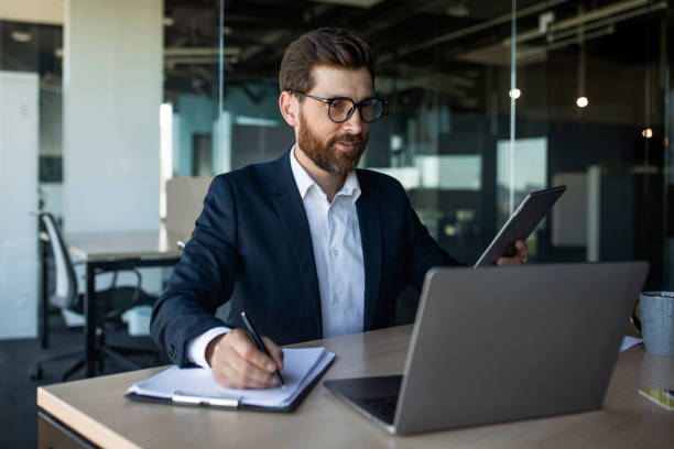 istock Male office manager in suit sitting at workdesk, taking notes while attending business webinar online 1478505414