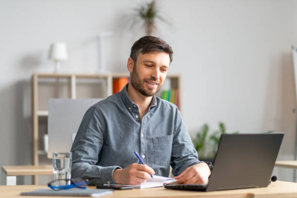 istock Happy mature entrepreneur man taking notes and using laptop, sitting at his workplace in office, copy space 1478505478