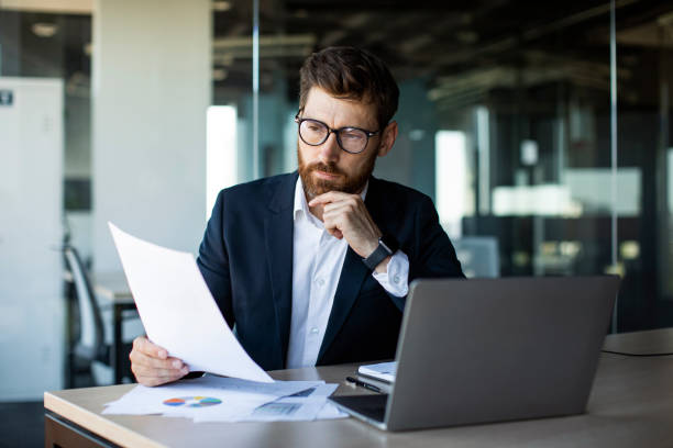 istock Busy mature businessman with beard in suit working with documents in office, sitting at workplace 1478505609