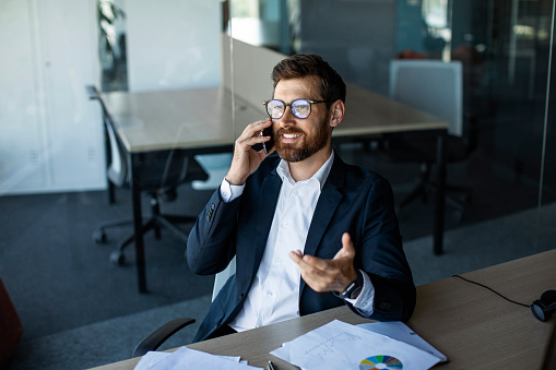 Corporate communication. Male entrepreneur talking on cellphone, sitting at workplace and having phone conversation, speaking with client discussing project, free space