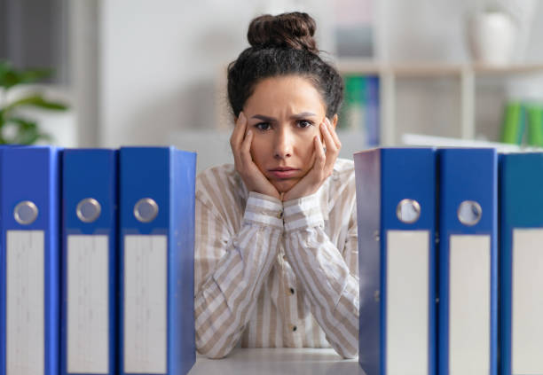 upset lady businesswoman sitting at workplace with stack of folders and looking at camera, feeling tired - overstrained imagens e fotografias de stock