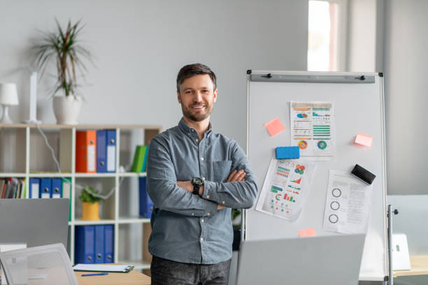 istock Confident mature businessman making project presentation, demonstrating graphs on whiteboard in office 1478505869