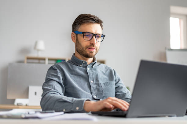 istock Focused mature businessman working with laptop computer at his desk in office, typing on pc keyboard, checking email 1478506011