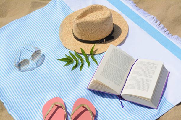 istock Beach towel with book, straw hat, sunglasses and flip flops on sand 1478508278