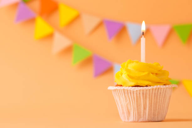 istock Tasty birthday cupcake with candle on orange table against party flags. Space for text 1478510909
