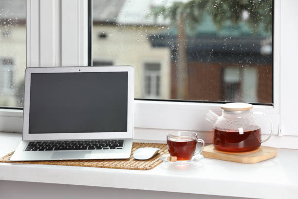 istock Modern laptop and tea on white sill near window 1478511448