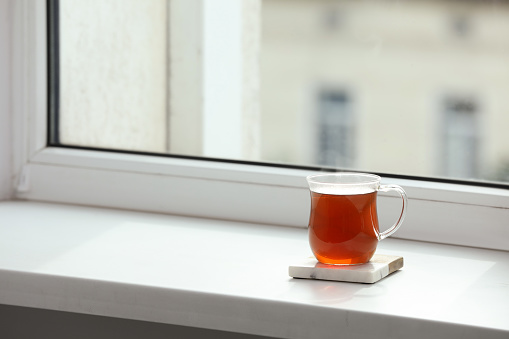 Cup of hot tea on white sill near window. Space for text