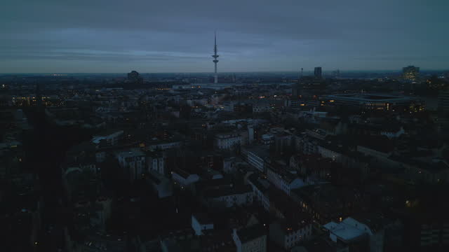 Forwards fly above buildings in residential urban borough at dusk. Heading towards tall TV tower. Hamburg, Germany
