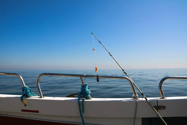 a spinning rod for catching fish is strung on the railing of a fishing boat against the background of the blue sea and sky - recreational boat nautical vessel fishing rod motorboat imagens e fotografias de stock
