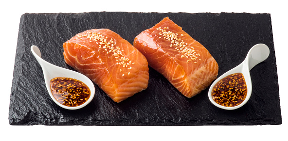 Two pieces of raw salmon fillet and special sesame sauce together on slate.
