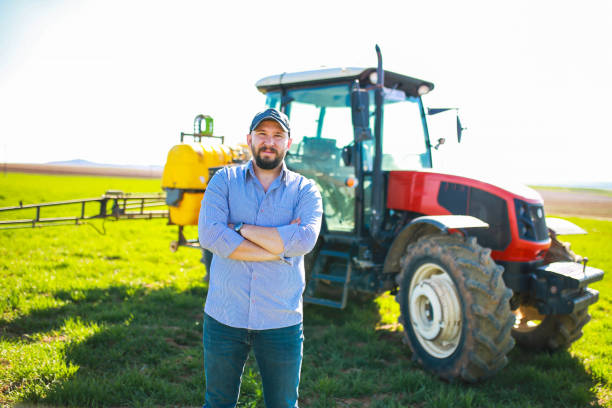 istock happy young farmer with arms folded in front of red tractor 1478534459
