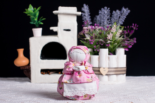 A bouquet of lavender and an oberezhnitsa doll. antique white stove, handmade cloth doll on a black background
