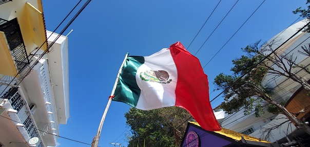 On a bright sunny day the Mexican flag waves against a blue sky over Avenida Quinta in Playa del Carmen, Mexico.