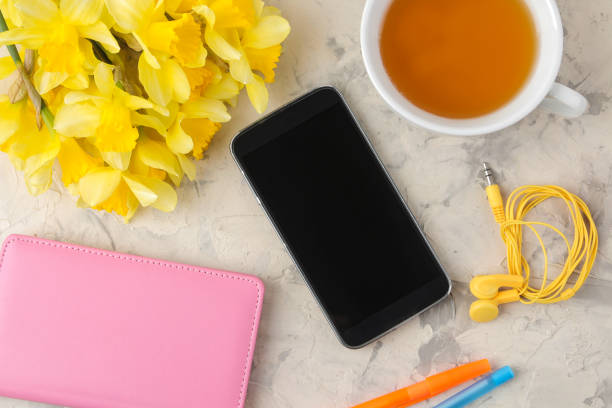 Spring flowers, yellow daffodils and a cup, tea, notepad, phone on a light concrete background. top view