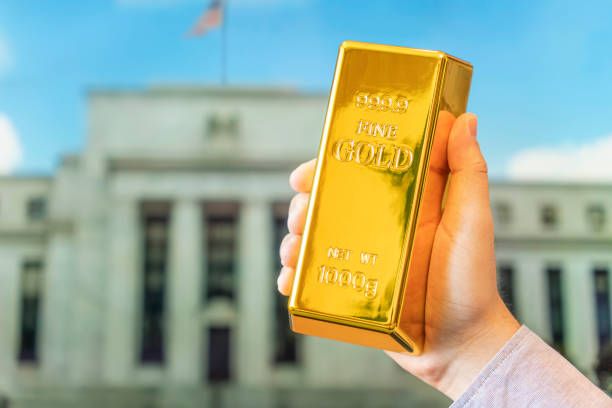 lingotto d'oro nella mano di un uomo sullo sfondo della banca centrale, il sistema della federal reserve degli stati uniti. - in gold we trust foto e immagini stock