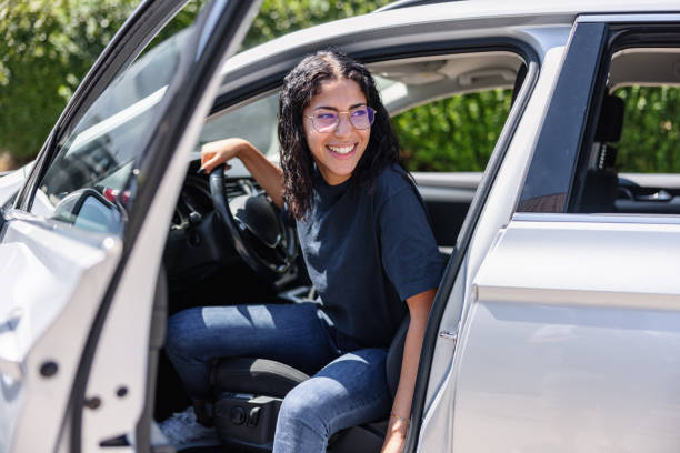 joven latina tratando de salir de un coche. ella se ríe - coche doméstico fotografías e imágenes de stock