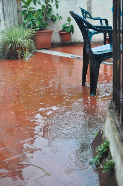 istock rain falling in a puddle on a patio with green chairs and plants in the background 1478565870