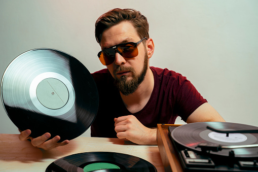 Bearded serious man, audiophile holding vinyl record in his hand, listening to music
