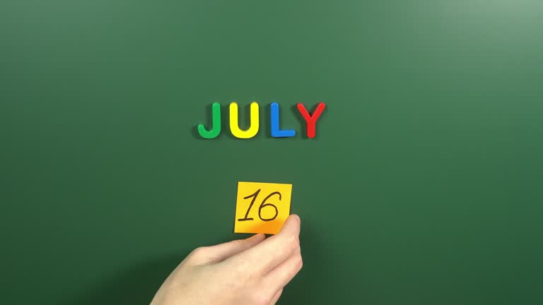 Hand sticking a sticker 16 July calendar day on school board. 16 date of July. Sixteenth day of July. 16th date number. 16 day calendar. Sixteen date. World Snake