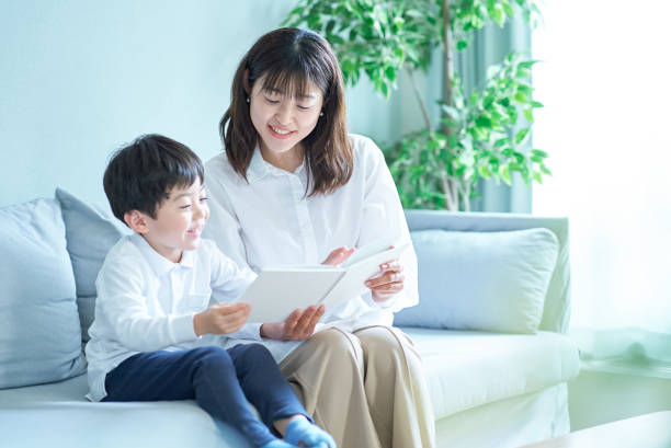 mãe e menino sentados e lendo livro ilustrado - japanese ethnicity family smiling happiness - fotografias e filmes do acervo