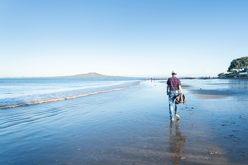 People walking and playing on the wet sandy beach with Rangitoto Island in the background, Milford, Auckland.
