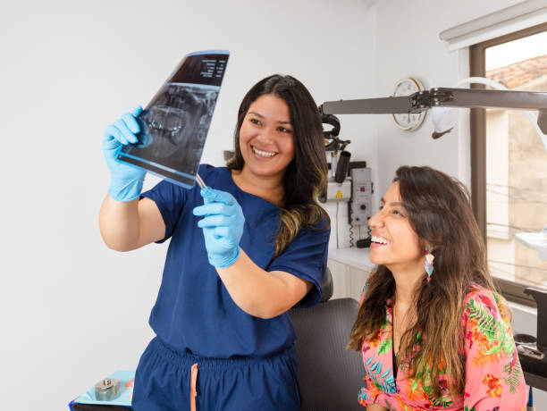 eine erfahrene zahnärztin lächelt ihre patientin in der praxis an, während sie ein panorama-röntgenbild zur untersuchung zeigt - dentist dentist office patient discussion stock-fotos und bilder