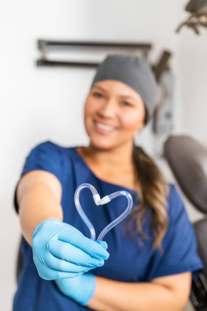 un dentista sorridente tiene due eiettori a forma di cuore in primo piano del suo studio dentisticodonne dentiste sorridenti che tengono due eiettori a forma di cuore nel suo ufficio - igienista dentale foto e immagini stock