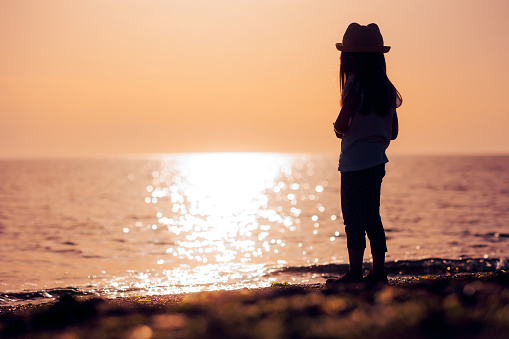 Little kid standing and admiring the beautiful seascape during sunrise