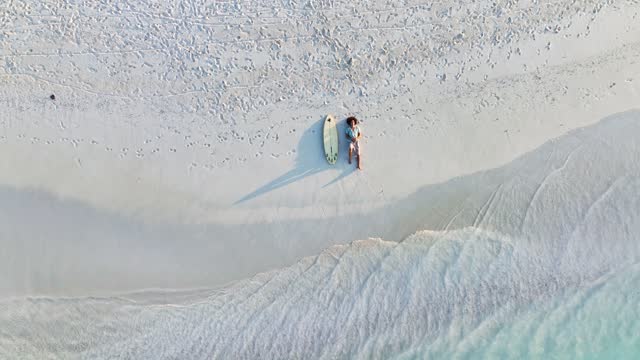 Aerial top upward shot of surfer lying on the beach with his surfboard