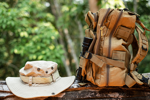 Bucket Hat and backpack hiking with a flashlight resting on wooden timber in the background is a forest