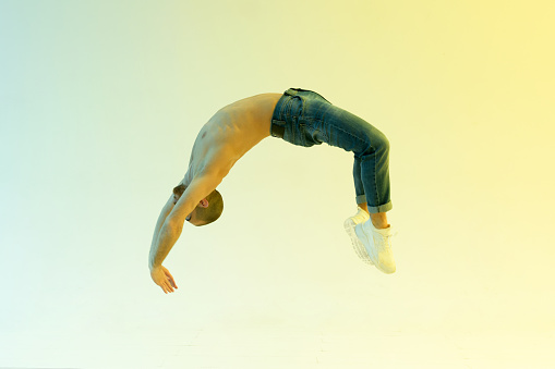 Fit male athlete performing a flick flack jump or back handspring in a full length side view over a colorful studio background