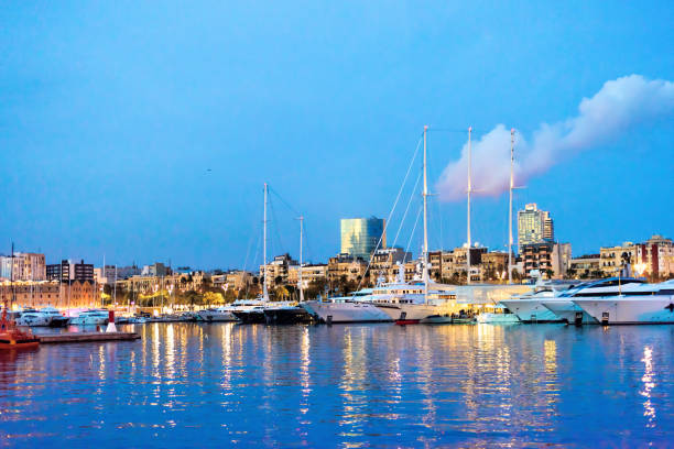Night harbor scene in Barcelona - Spain. Reflections in calm water, modern architecture, and a red-lit tower add contrast and maritime atmosphere.
