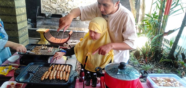 Father and daughter is cooking sausages in lunch barbeque at home.