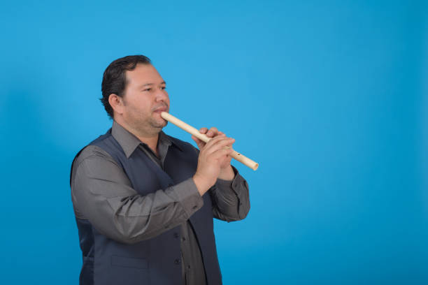 Studio portrait of a man playing a recorder. Blue background with copy space.