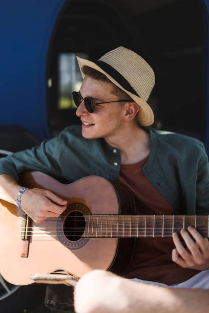 istock Young man sitting in van playing on the guitar and enjoying summer time. 1478642741