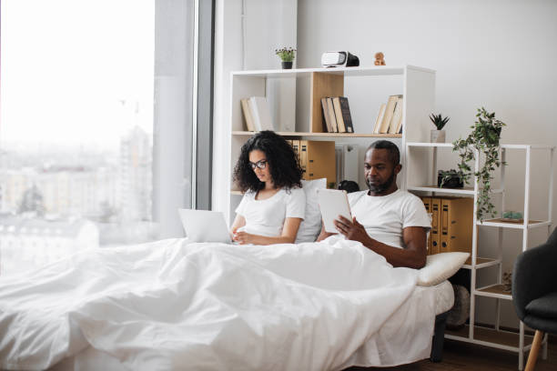 istock Romantic partners lounging on bed with electronic devices 1478648221