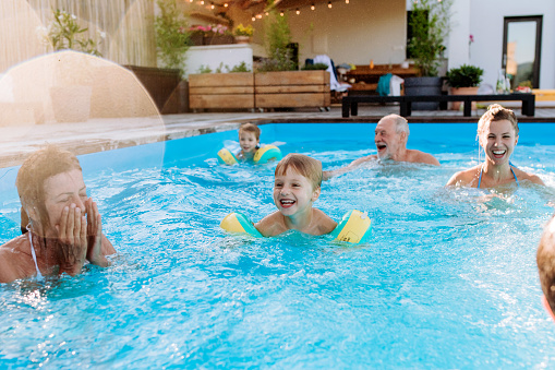 A multi generation family having fun and enjoying swimming in backyard pool.