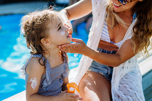 Young mother applying a sunscreen lotion to her daughter. Safety sunbathing in hot day.