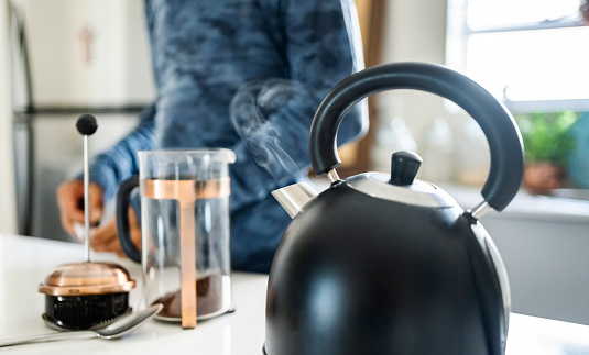 Steaming kettle on stove in kitchen with a person preparing coffee in background