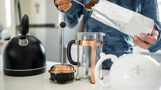 Cropped shot of a person adding a spoon of coffee powder in french press coffee maker on kitchen table