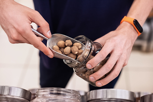 A man in supermarket filling a glass jar with spices, ecology idea