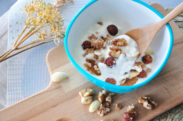 Top view of plain yogurt with mixed nuts bowl on wooden board