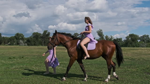 Twin Sisters in Summer Dresses, One Rides Horse, the Other Leads a Horse Nearby