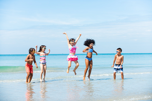 Group of Diversity little child boy and girl friends playing in the ocean at tropical beach together on summer vacation. Happy children kids enjoy and fun outdoor lifestyle travel ocean on beach holiday.