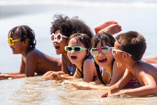 Group of Diversity little child boy and girl friends lying on tropical beach and playing sea water together on summer vacation. Happy children kids enjoy and fun outdoor lifestyle on beach holiday.