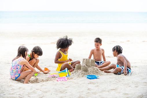 Group of Diversity little child boy and girl friends playing beach toy and build a sand castle together at tropical beach. Children kids enjoy and fun outdoor lifestyle travel ocean on summer holiday vacation.