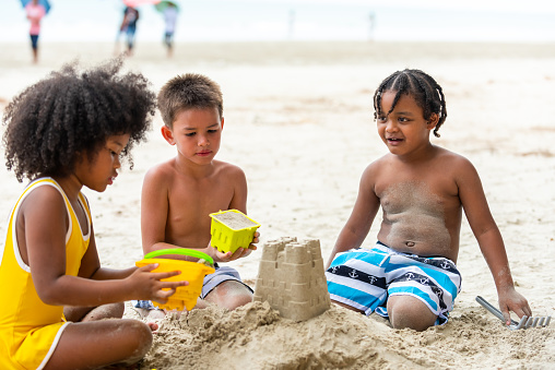 Group of Diversity little child boy and girl friends playing beach toy and build a sand castle together at tropical beach. Children kids enjoy and fun outdoor lifestyle travel ocean on summer holiday vacation.