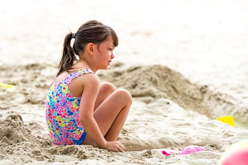 Little Asian child girl in swimsuit playing beach toy and build a sand castle at tropical beach in sunny day. Children kid having fun outdoor activity lifestyle travel ocean on summer holiday vacation.